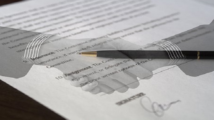 un contrat et un stylo avec deux mains pour passer un accord en arrière-plan - contrat d'externalisation - Buro Services 
