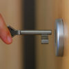 une main tenant une clé devant une serrure de porte - domiciliation commerciale - Buro Services