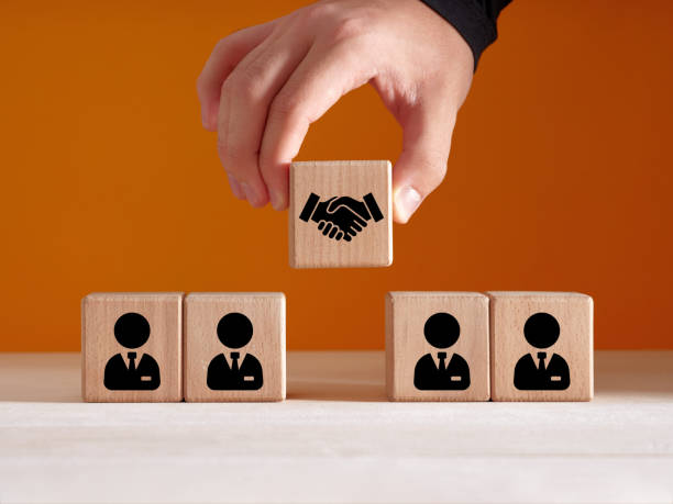 La main d'un homme pose des cubes en bois avec des icônes représentant un homme d'affaires et une poignée de main - mission portage salarial juridique - Buro Services