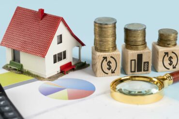 une maquette de maisons et des piles d'argent sur une table - coût réel d'une domiciliation d'entreprise - Buro Services