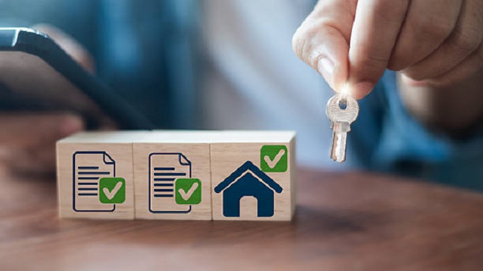 Main tenant une clé de maison, avec des icônes de liste de contrôle de documents - services de domiciliation - Buro Services